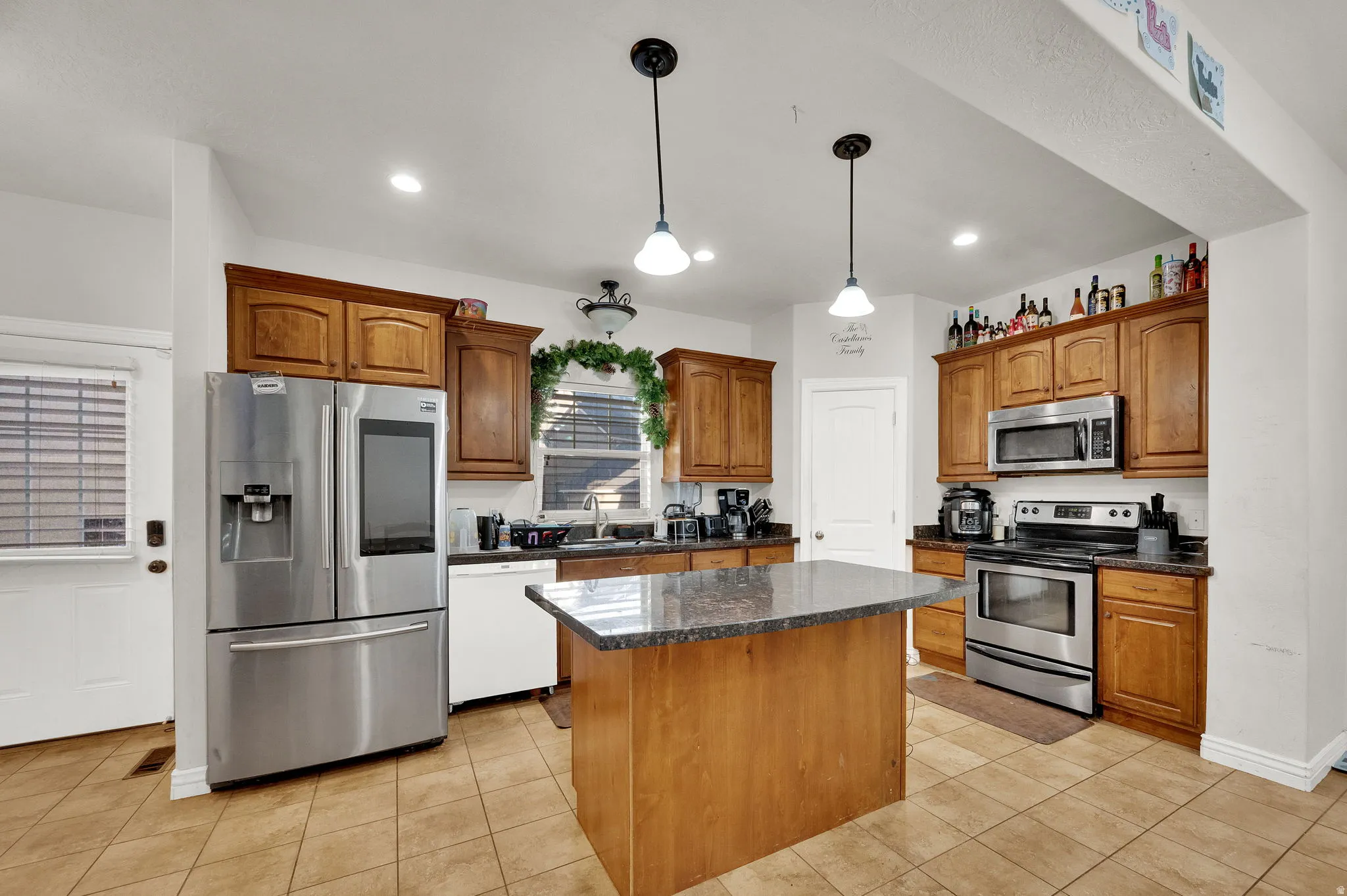 Kitchen featuring stainless steel appliances, decorative light fixtures, wood finish cabinets, and light tile patterned floors