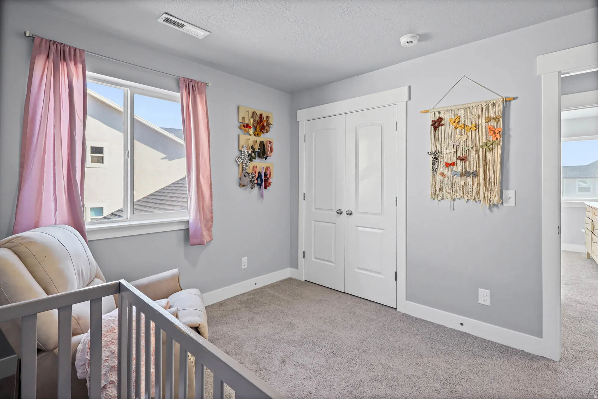 Bedroom featuring light carpet, a nursery area, a closet, and a textured ceiling