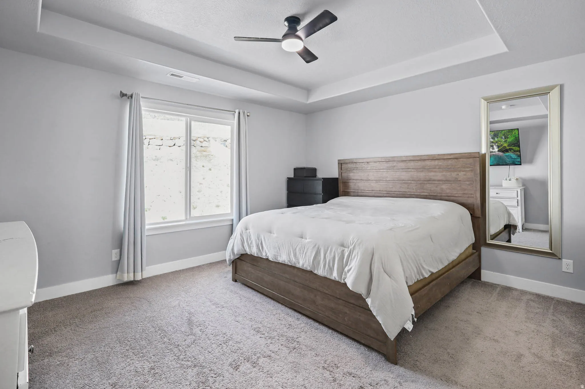 Primary Bedroom with a raised ceiling, light colored carpet, and ceiling fan