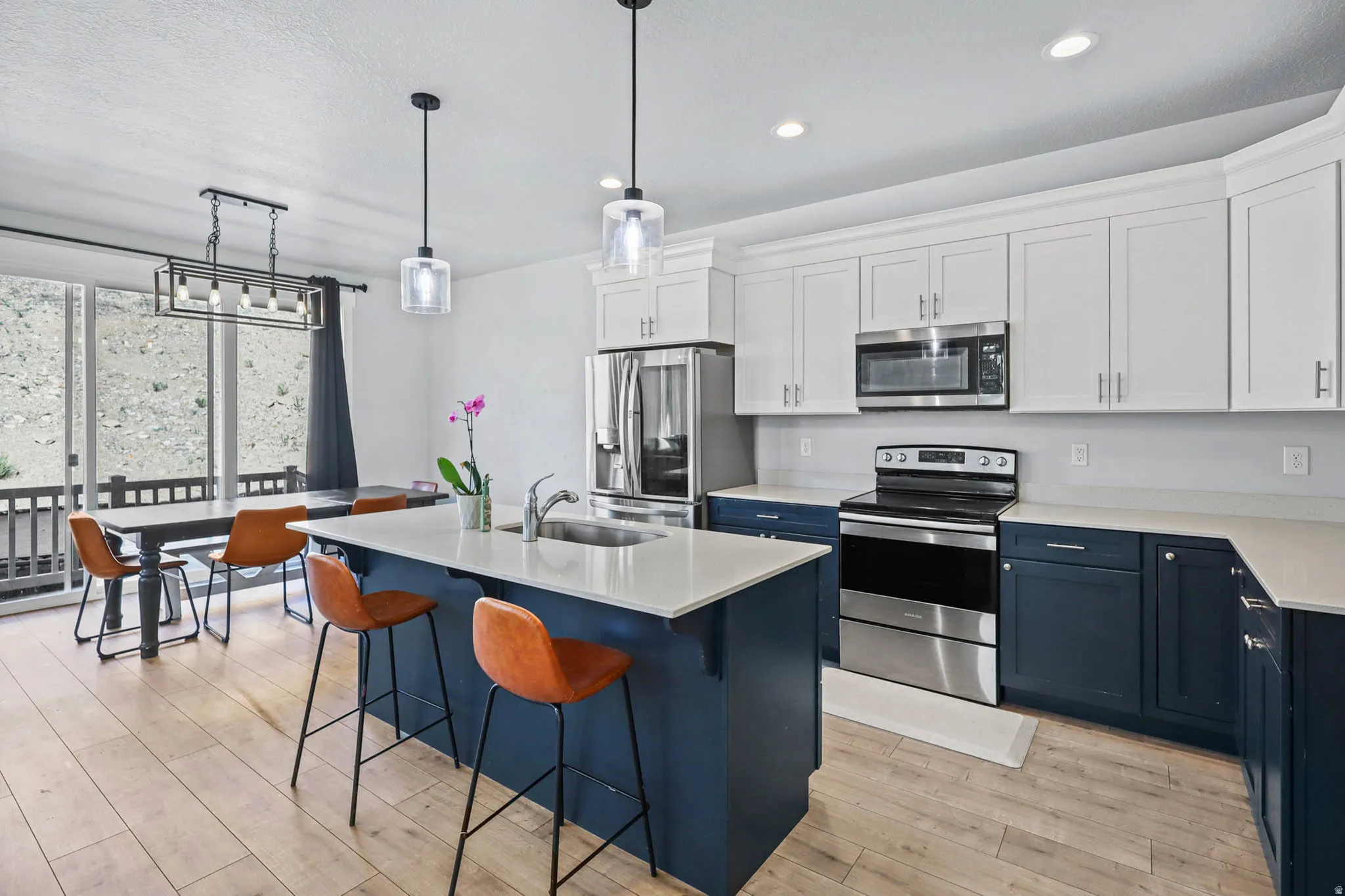Two tone kitchen featuring stainless steel appliances, dual tone cabinets, decorative light fixtures, a center island with sink, and light wood-type flooring