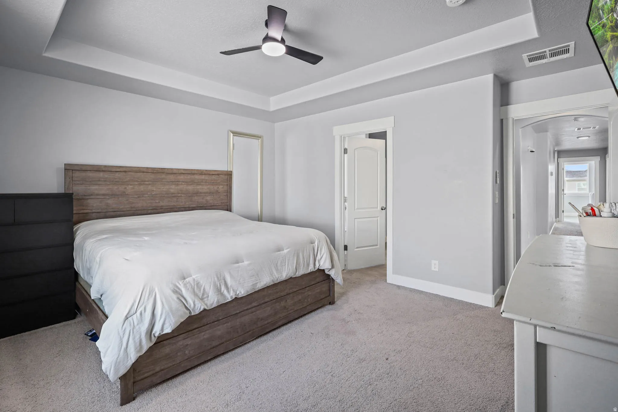 Primary Bedroom featuring a tray ceiling, light colored carpet, and ceiling fan