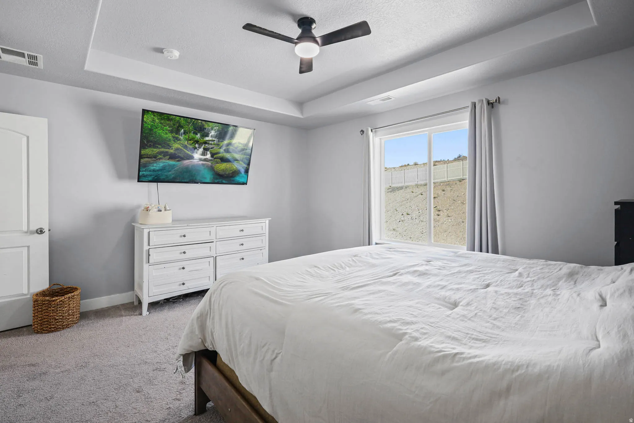 Primary Bedroom featuring a raised ceiling, carpet flooring, a textured ceiling, and ceiling fan