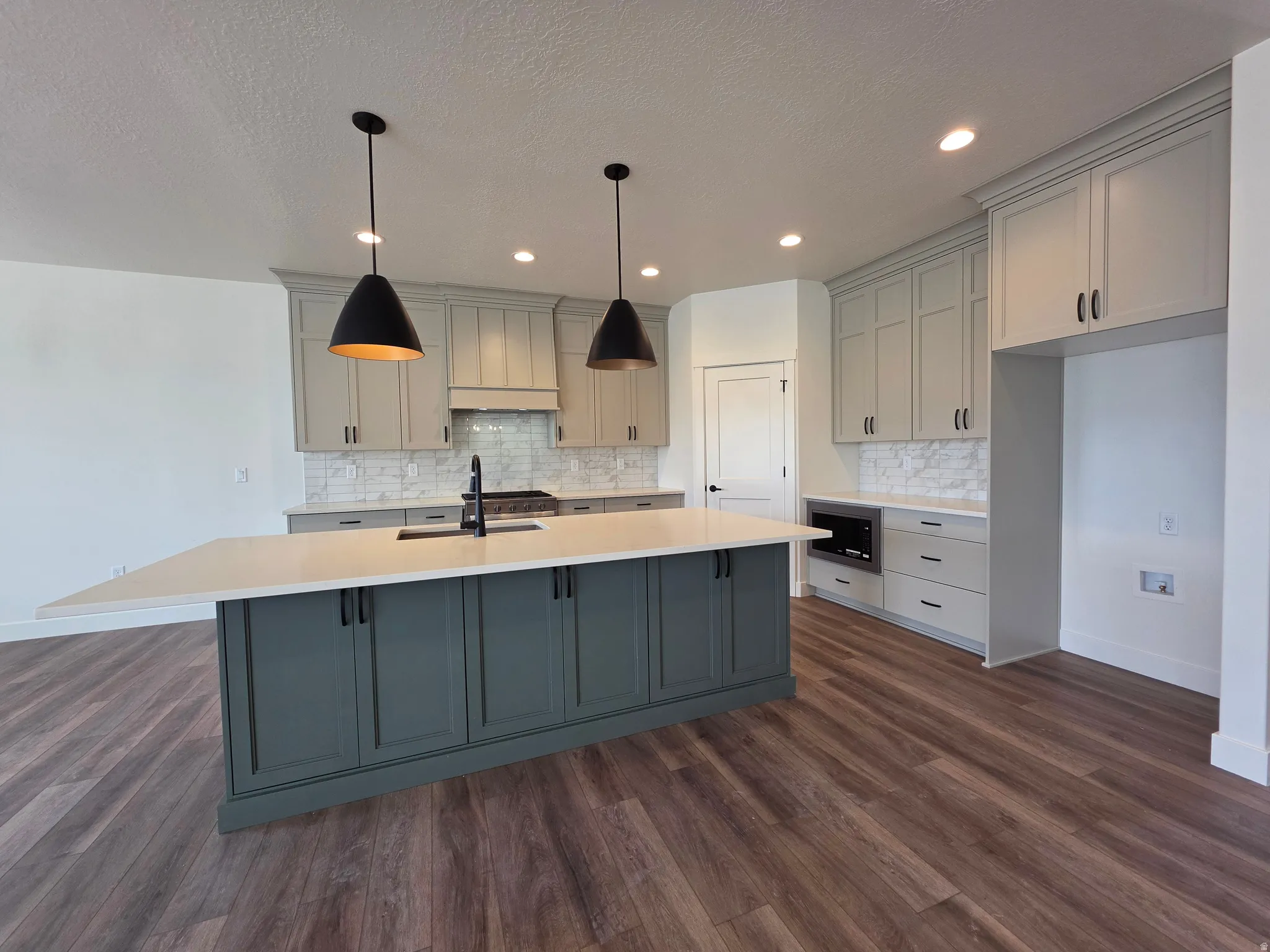 Spacious kitchen featuring a large island with a countertop extension, light-colored perimeter cabinetry, and wood-finish flooring
