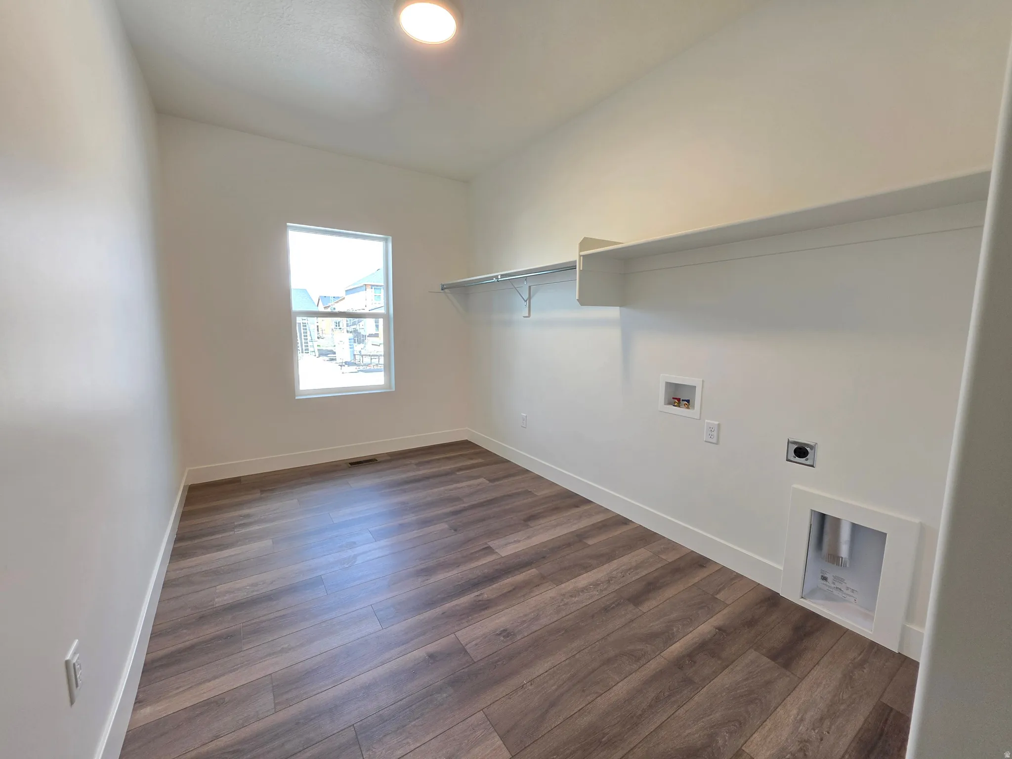 Laundry room with wood-finish flooring, a window, built-in shelving, and utility hookups