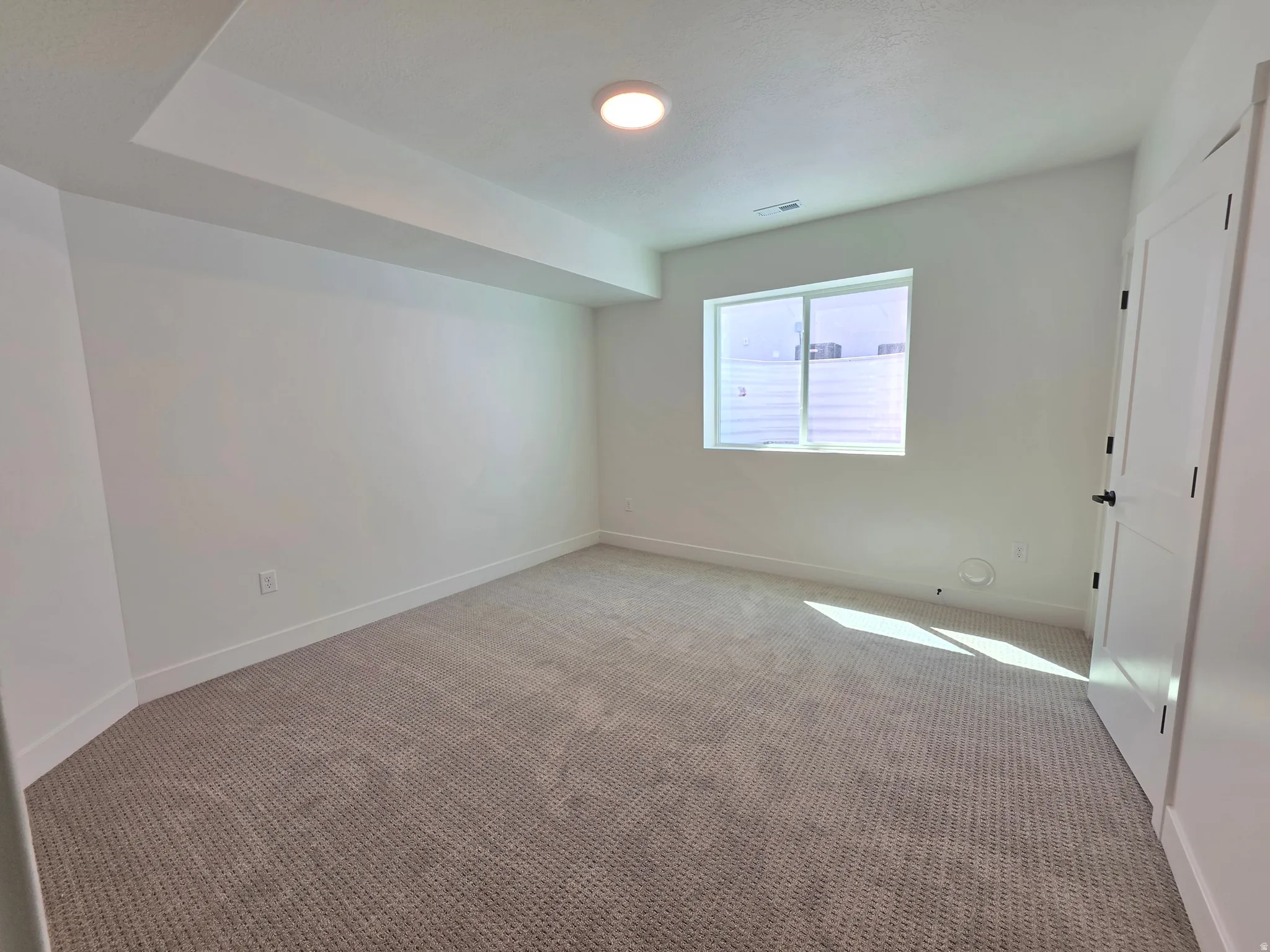 Carpeted room featuring a single window with blinds, a white paneled door with black hardware, and a recessed ceiling light