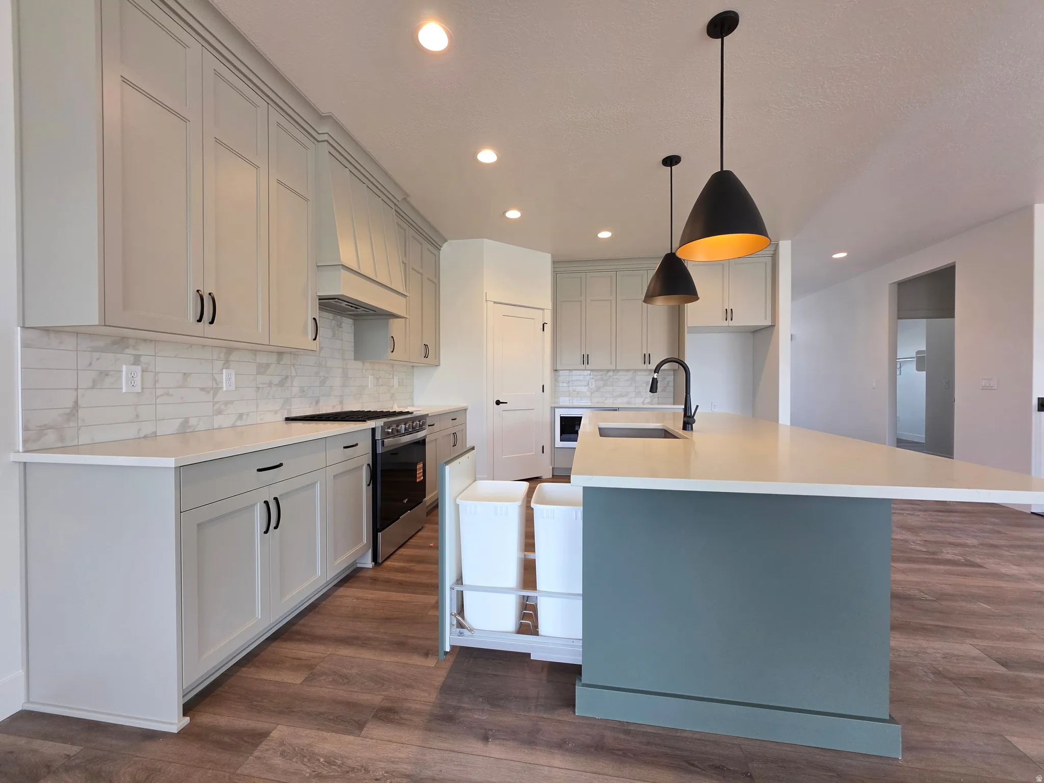 Modern kitchen featuring light gray shaker cabinetry, wood-finish flooring, a white subway tile backsplash, and recessed lighting