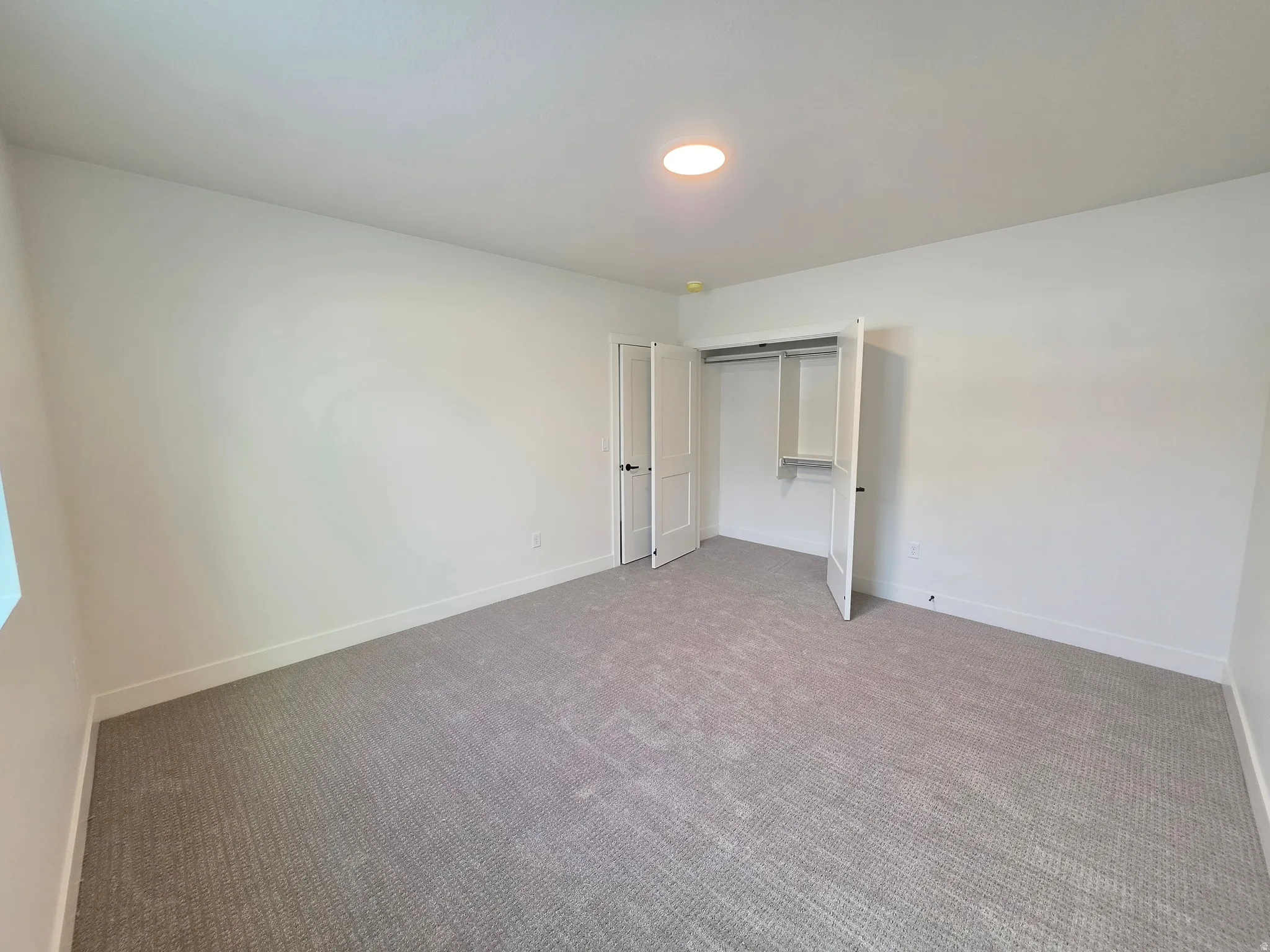 Spacious room featuring neutral carpeting, white walls, and a ceiling-mounted light fixture
