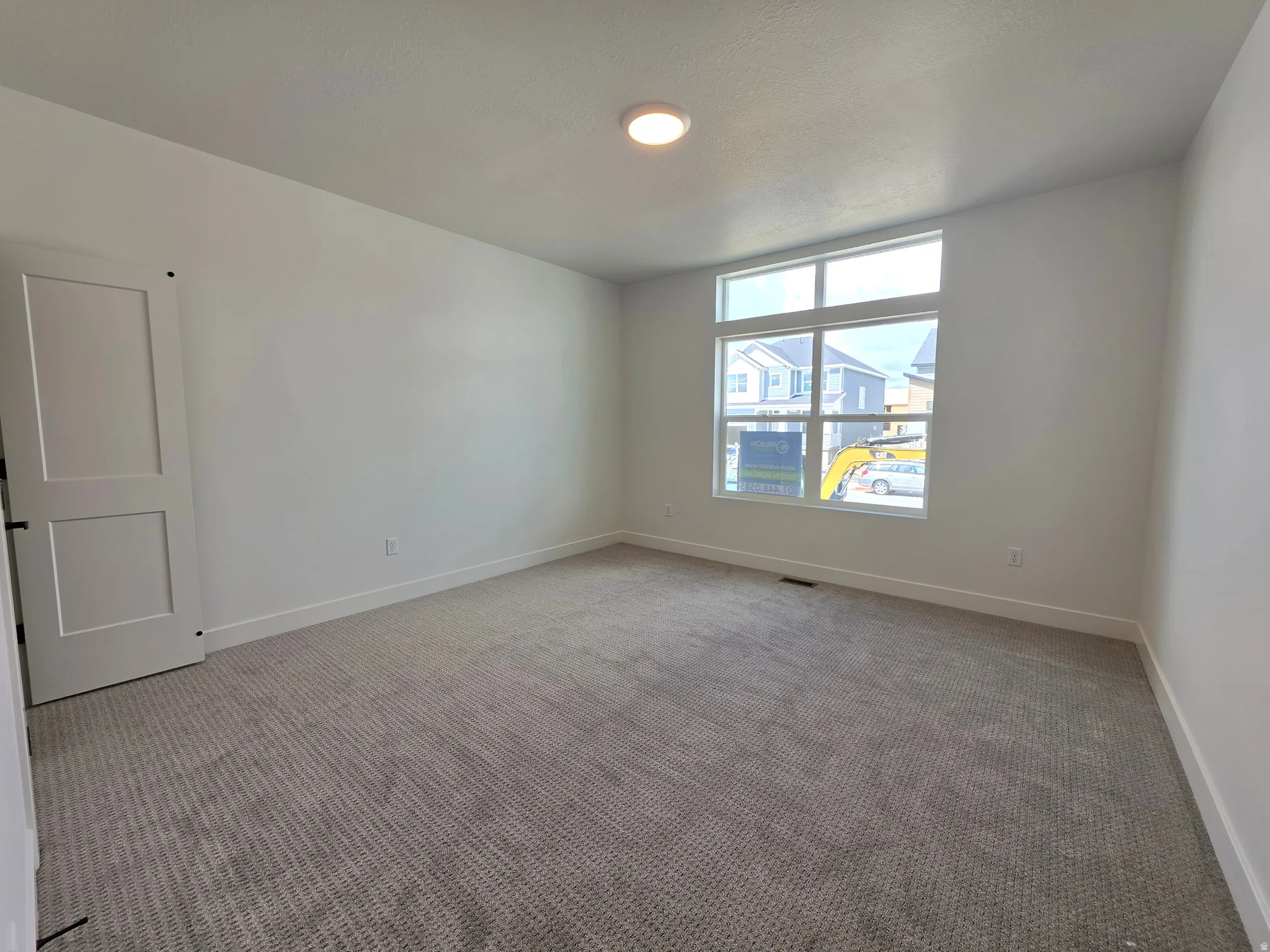 Spacious room featuring neutral carpeting, white walls, a contemporary window configuration with transom, a flush-mount ceiling light, and a two-panel door with matte black hardware