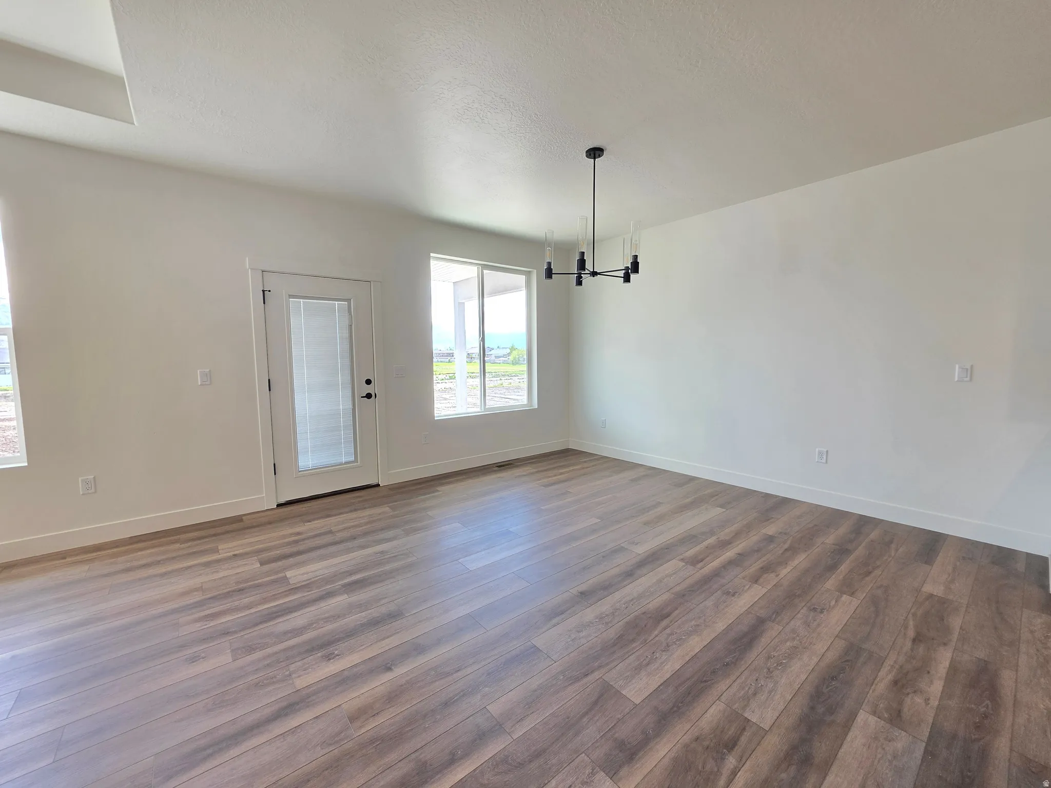 Expansive room featuring wood-finish flooring, white walls, and a contemporary chandelier