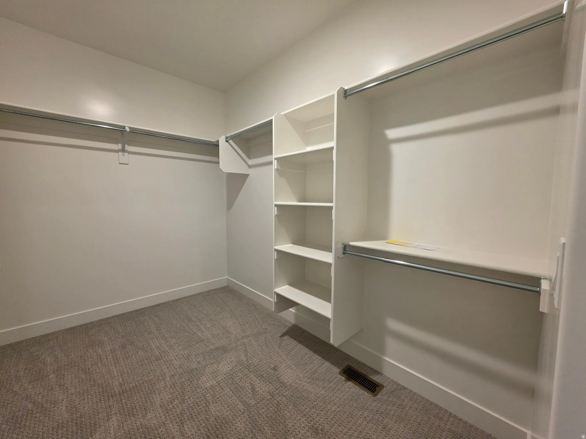 Walk-in closet with integrated shelving units, multiple chrome hanging rods, and neutral carpet flooring