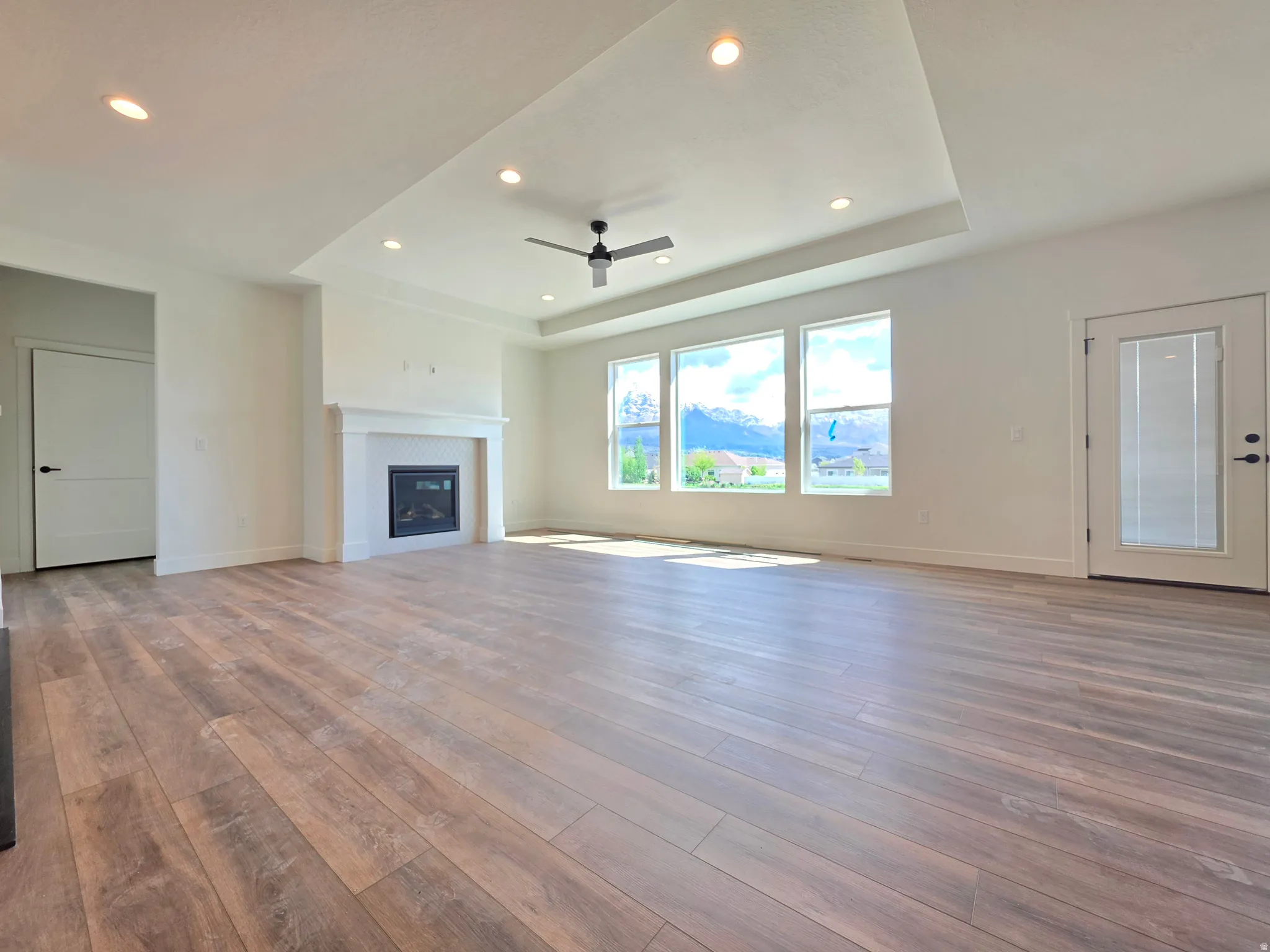Spacious living area featuring wood-finish flooring, a contemporary fireplace with tile surround, and a tray ceiling with recessed lighting
