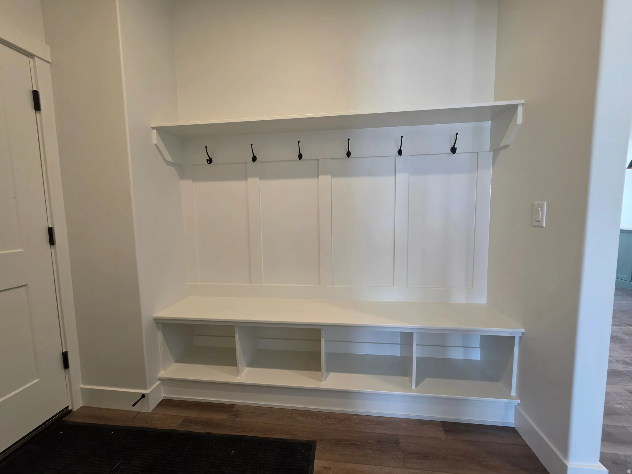 Built-in mudroom bench with three storage cubbies, five coat hooks, and an overhead shelf, set against a wainscoting-style wall paneling