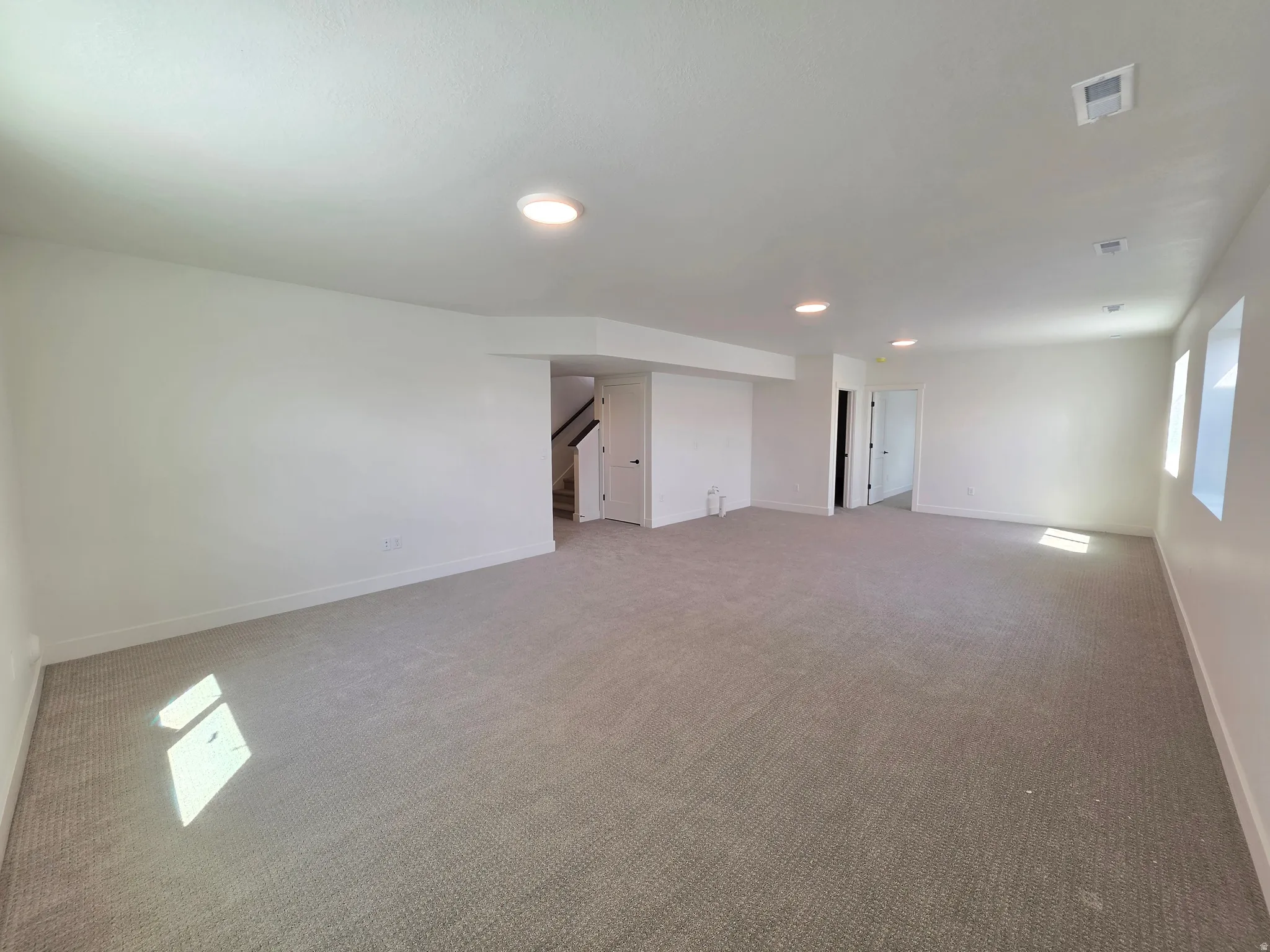 Spacious carpeted room featuring recessed lighting, multiple windows, white baseboards, and a neutral color palette
