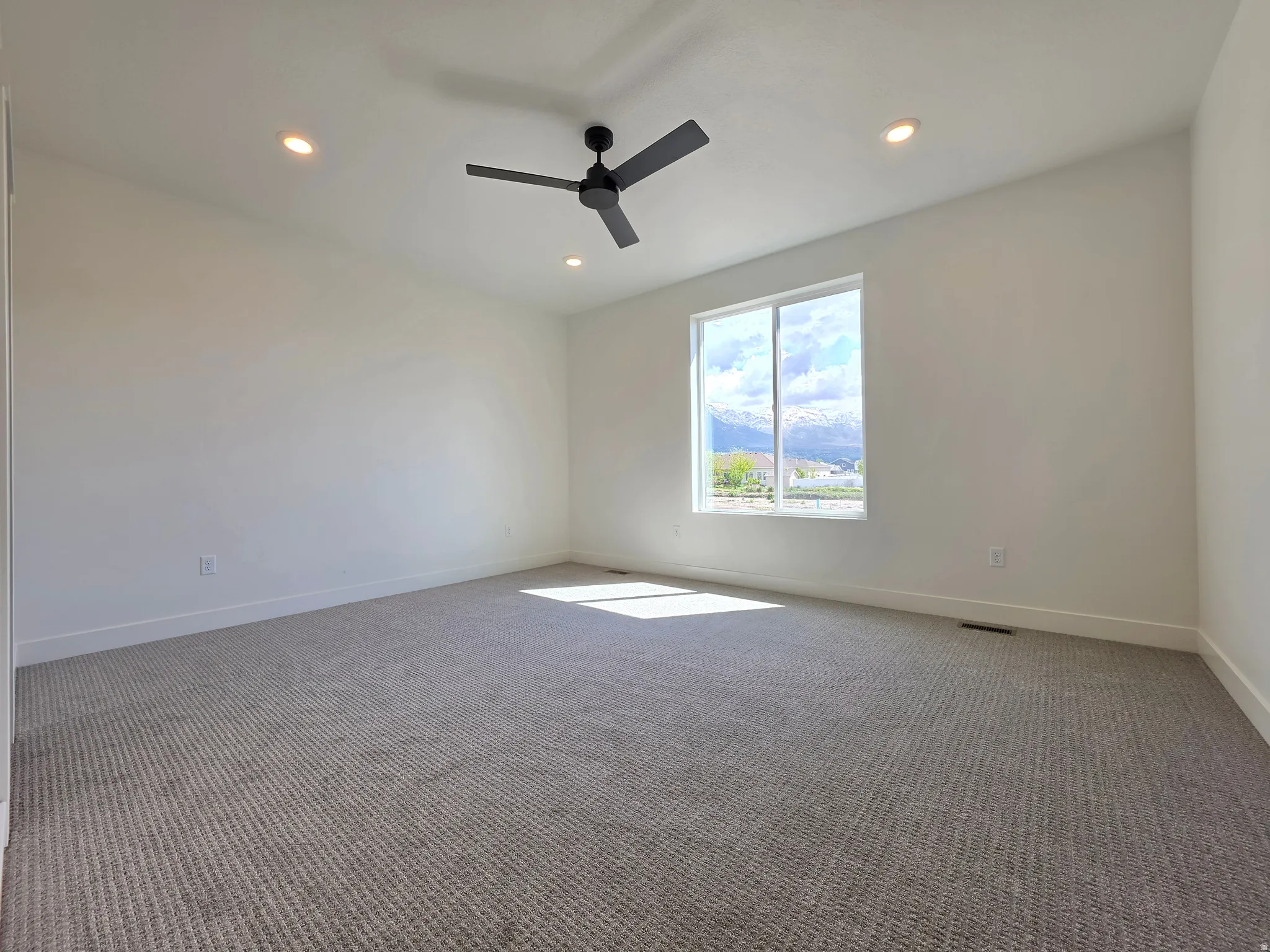 Spacious room featuring neutral carpeting, recessed lighting, and a modern ceiling fan
