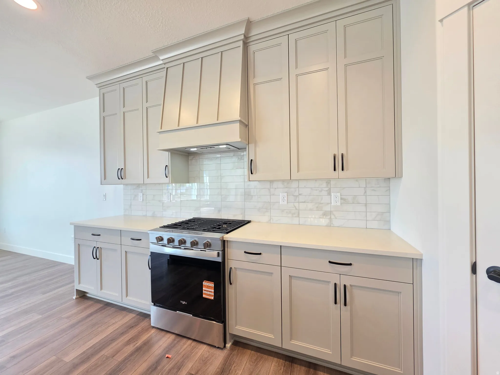 Modern kitchen featuring light-toned cabinetry with black hardware, a stainless steel range, and a decorative range hood