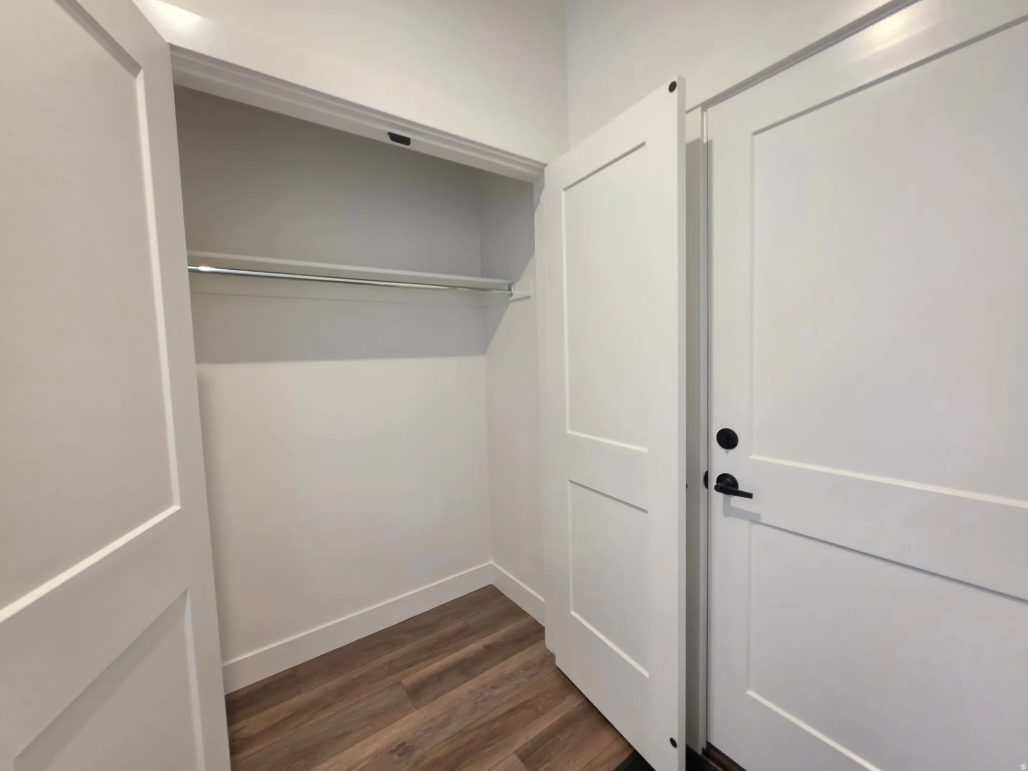 White two-panel interior doors with matte black hardware, wood-finish flooring, and white baseboards