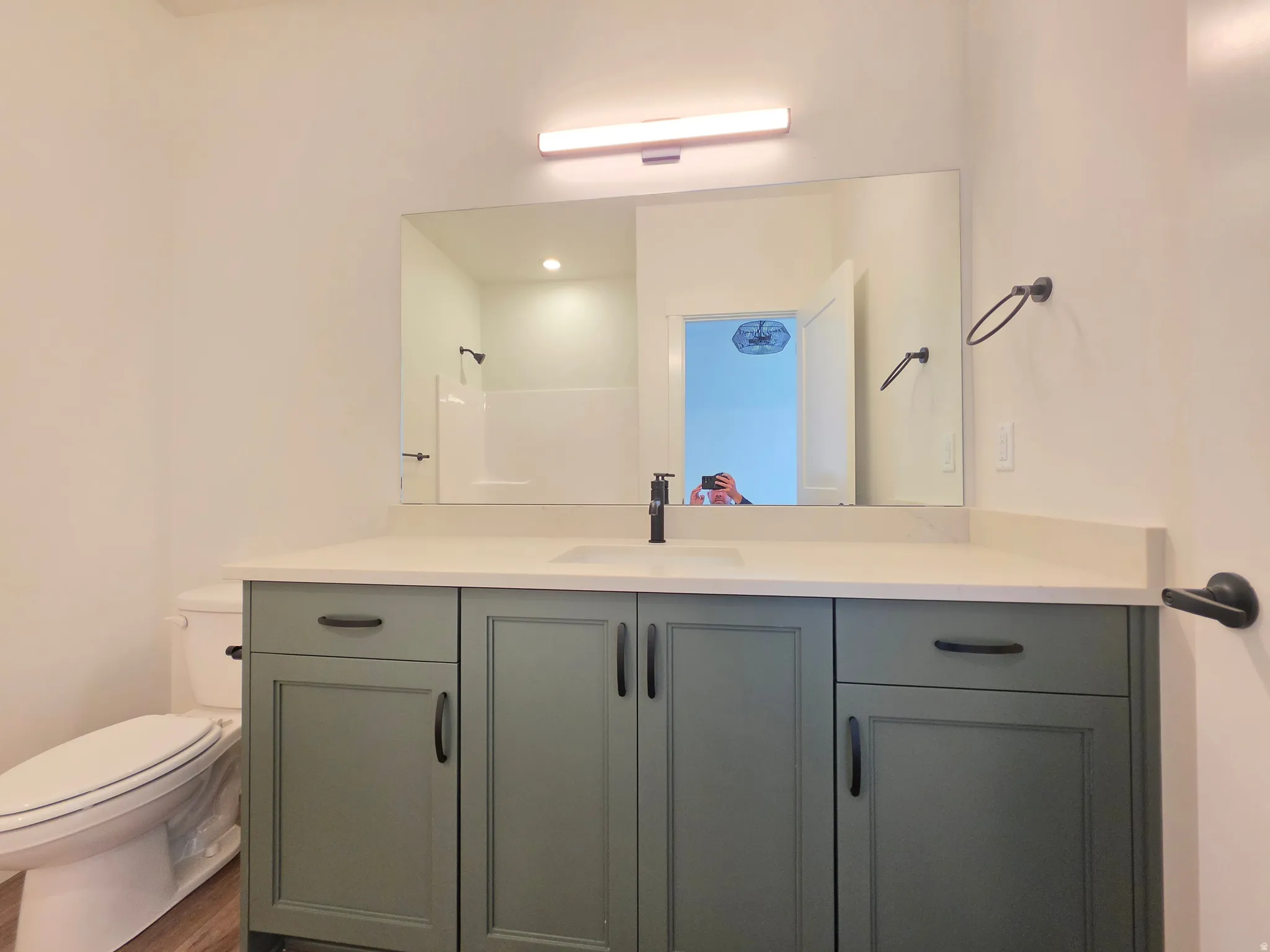 Bathroom featuring a sage green vanity with black hardware, a white countertop, and a rectangular mirror with overhead lighting