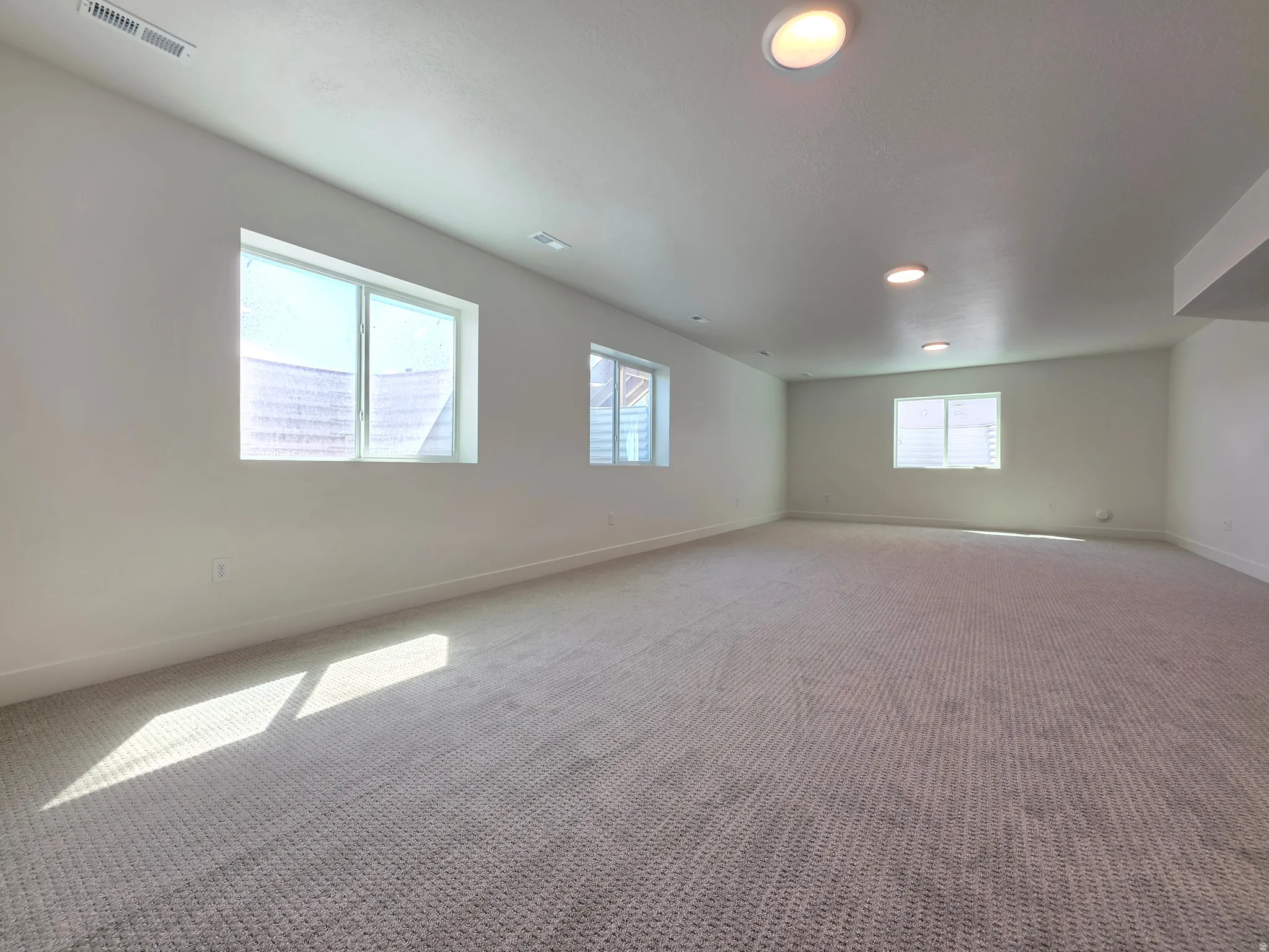 Spacious room featuring light-toned carpeting, white baseboards, and multiple recessed ceiling lights