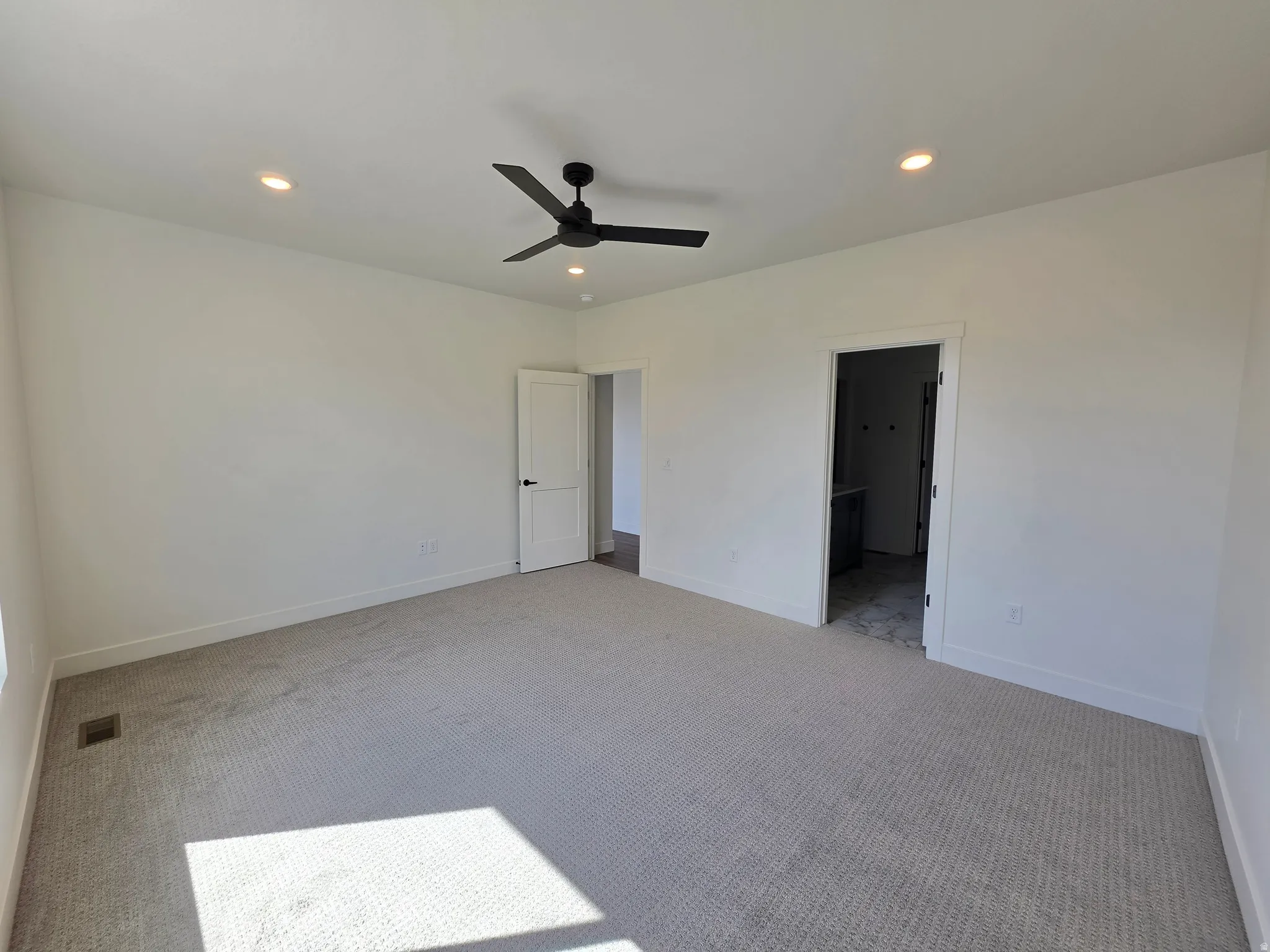 Spacious room featuring neutral carpeting, white walls, recessed ceiling lights, a black ceiling fan, and white trim