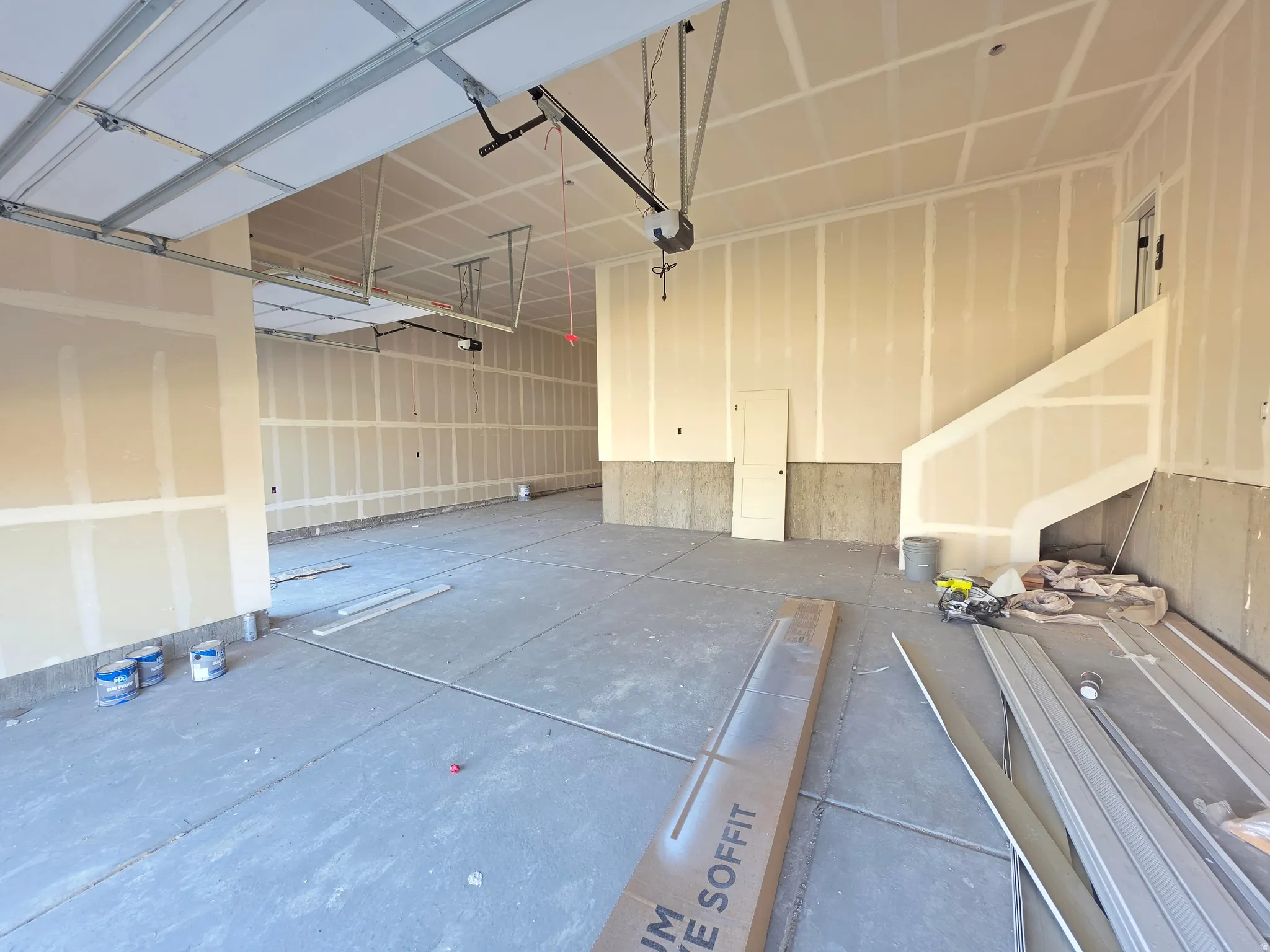 Spacious garage featuring a concrete floor, exposed ceiling joists, and a partial staircase