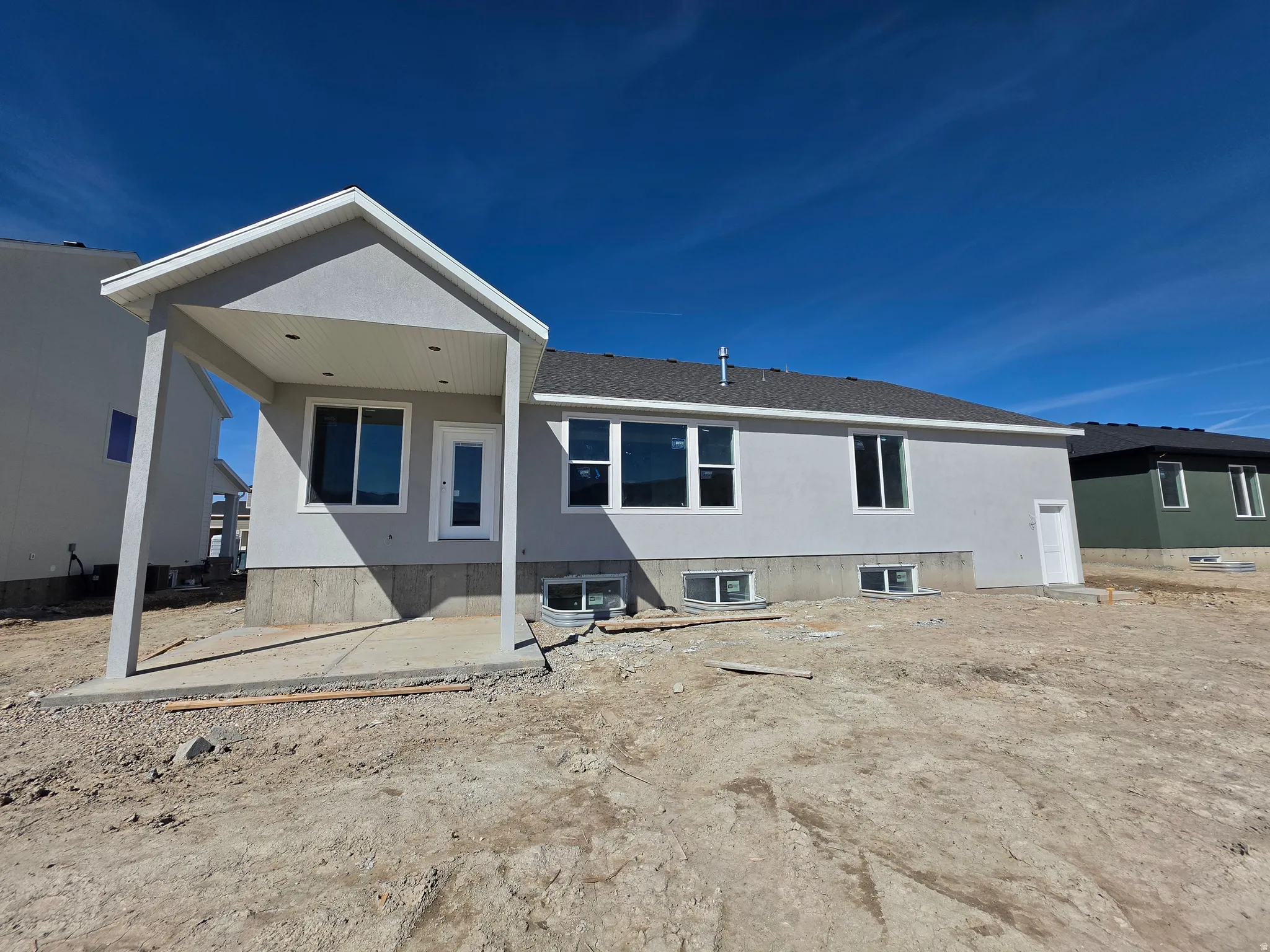 Contemporary stucco exterior featuring a covered patio, multiple windows, a rear entry door, and a basement access door