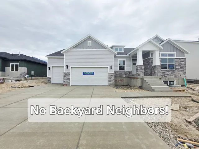 Light gray siding exterior with stone accents, a two-car garage, concrete driveway, and covered entry porch with white columns