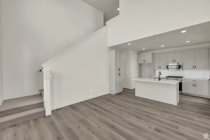 Kitchen with stainless steel appliances, a high ceiling, a center island with sink, decorative backsplash, and light wood-type flooring