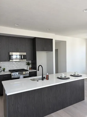 Spacious kitchen featuring a large central island with a white solid surface countertop, dark wood-finish cabinetry, stainless steel appliances, a subway tile backsplash, and recessed lighting