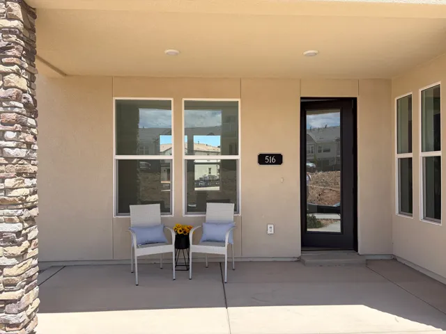 Covered front entry featuring a stacked stone column, smooth stucco exterior, and a contemporary glass-paneled entry door