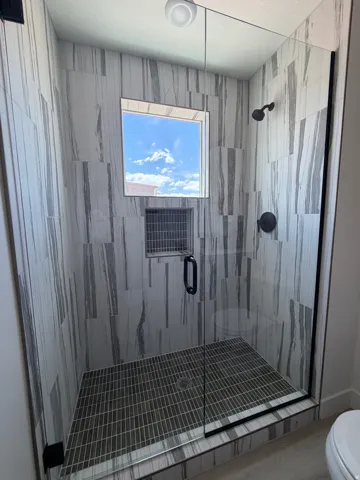 Glass-enclosed shower featuring large format tiled walls, a square window, and a built-in tiled niche