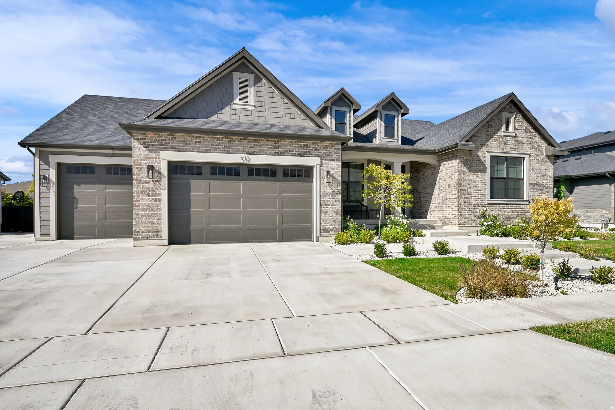 Craftsman inspired home featuring an attached garage, driveway, brick siding, a porch, and roof with shingles