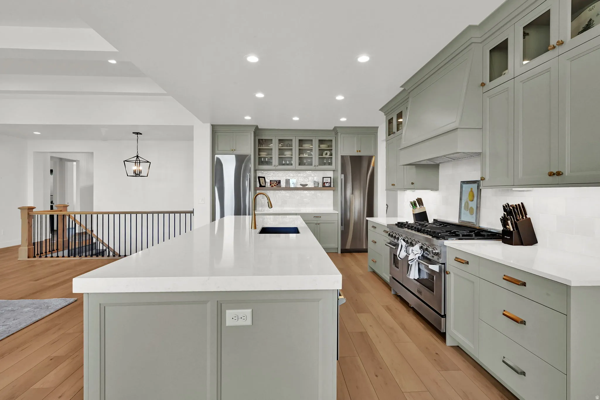 Kitchen with glass insert cabinets, stainless steel appliances, light wood-style flooring, light stone counters, and an island with sink