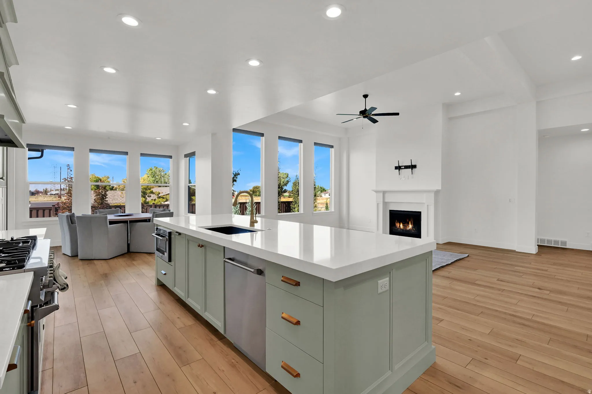 Kitchen with open floor plan, stainless steel appliances, a warm lit fireplace, a center island with sink, and recessed lighting