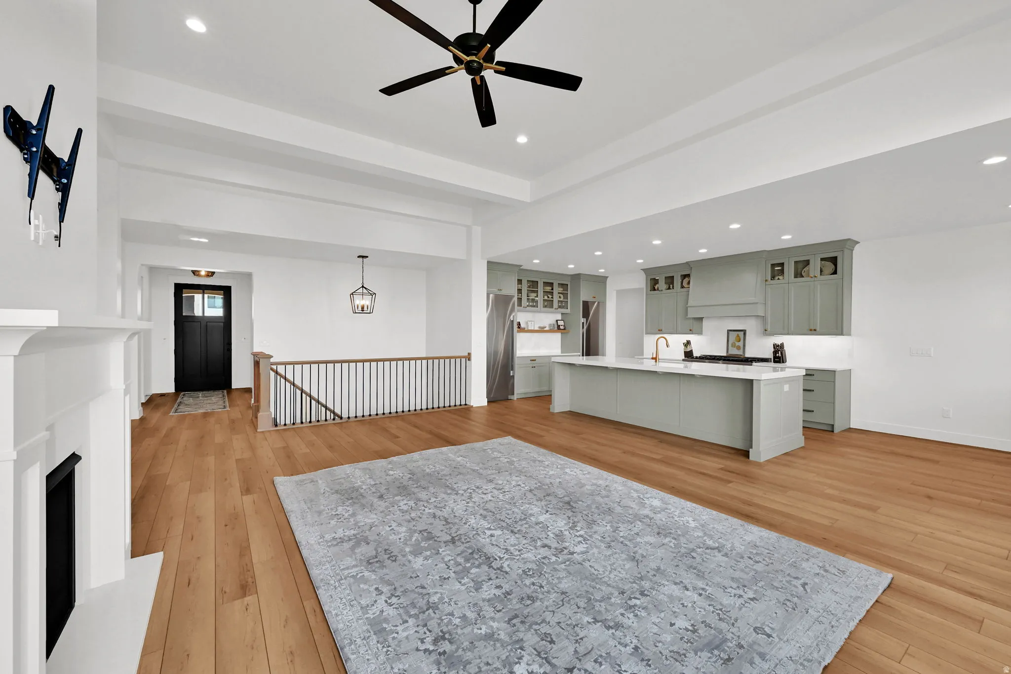 Living room with light wood finished floors, ceiling fan, a fireplace with raised hearth, and recessed lighting