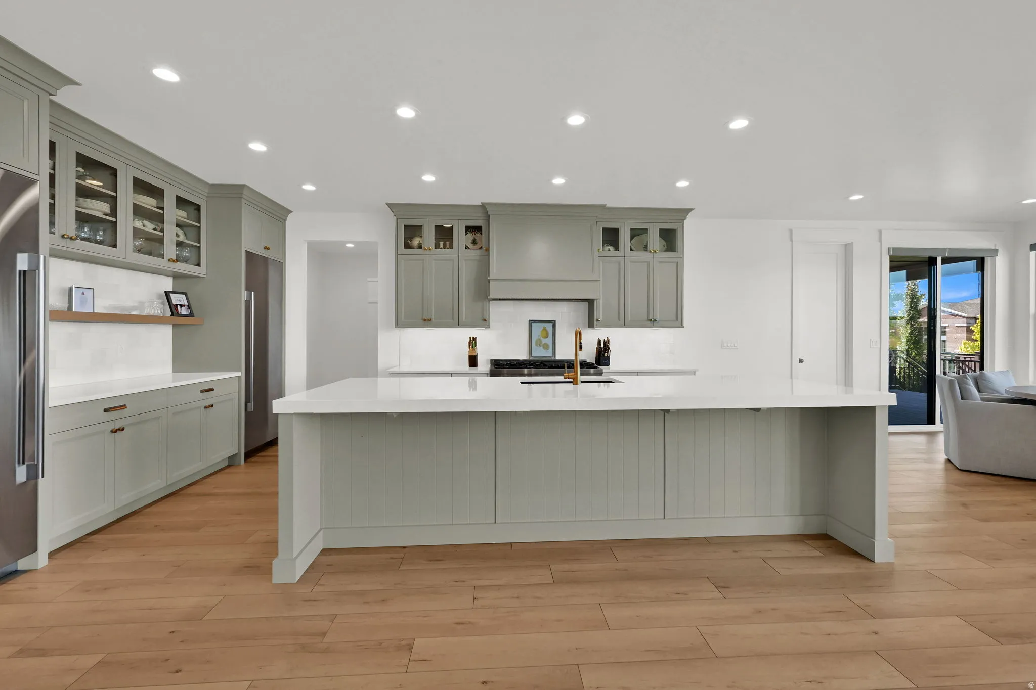 Kitchen with recessed lighting, light wood-style flooring, a spacious island, light stone countertops, and glass fronted cabinets