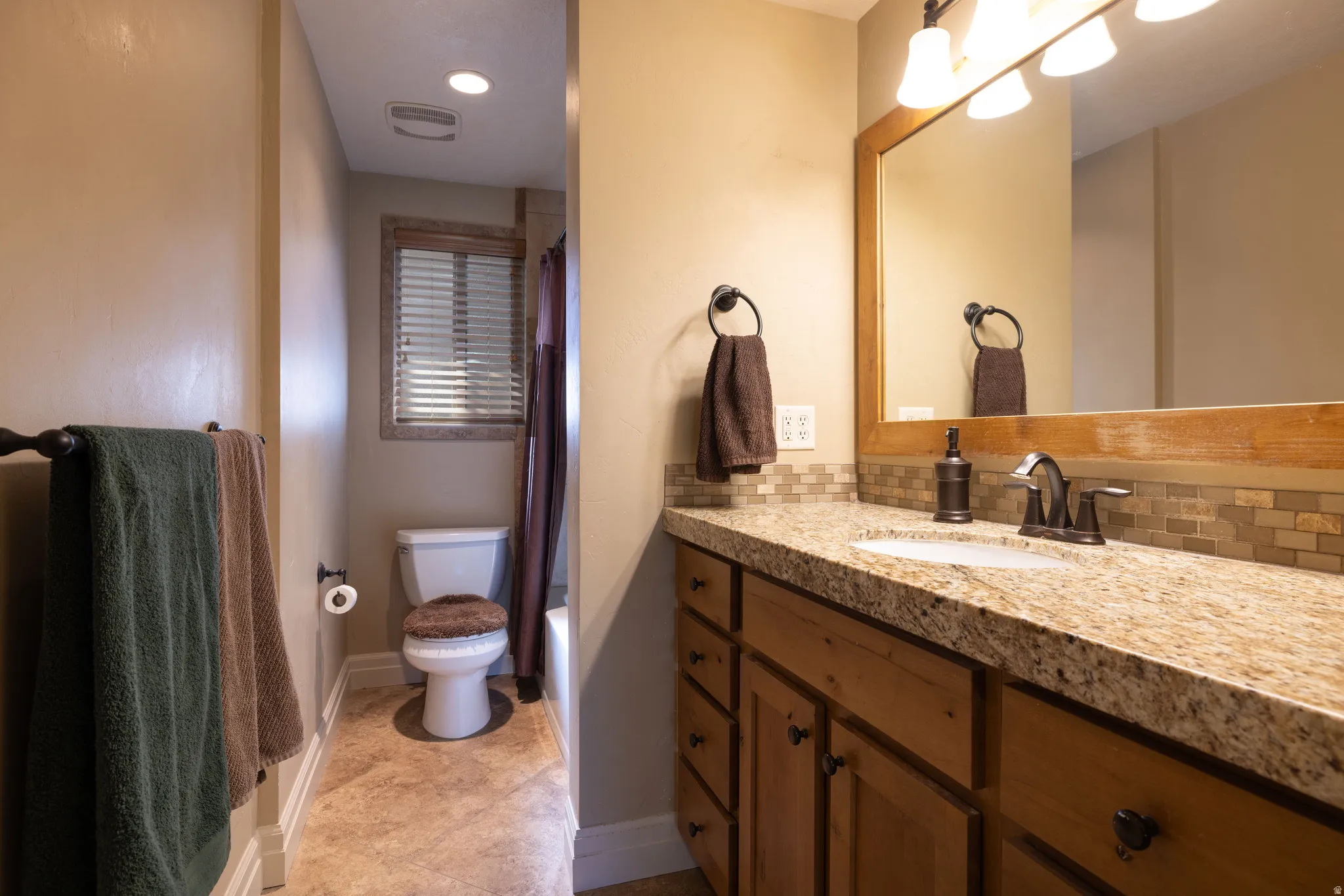 Full bath featuring vanity, shower / tub combo, backsplash, and light tile patterned flooring
