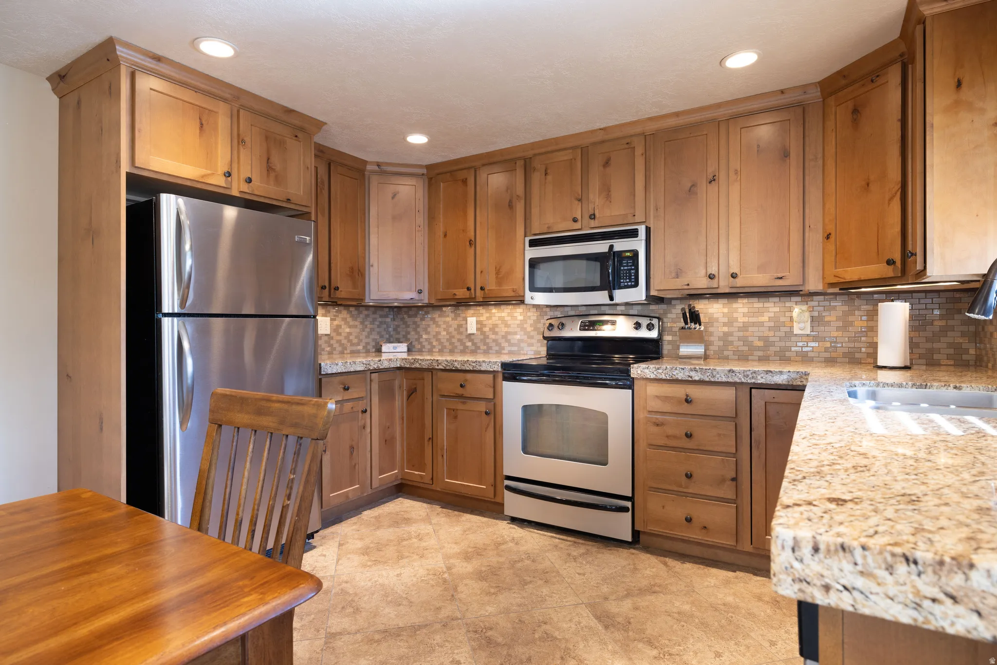 Kitchen with stainless steel appliances, granite counters, wood finish cabinets, recessed lighting, and backsplash