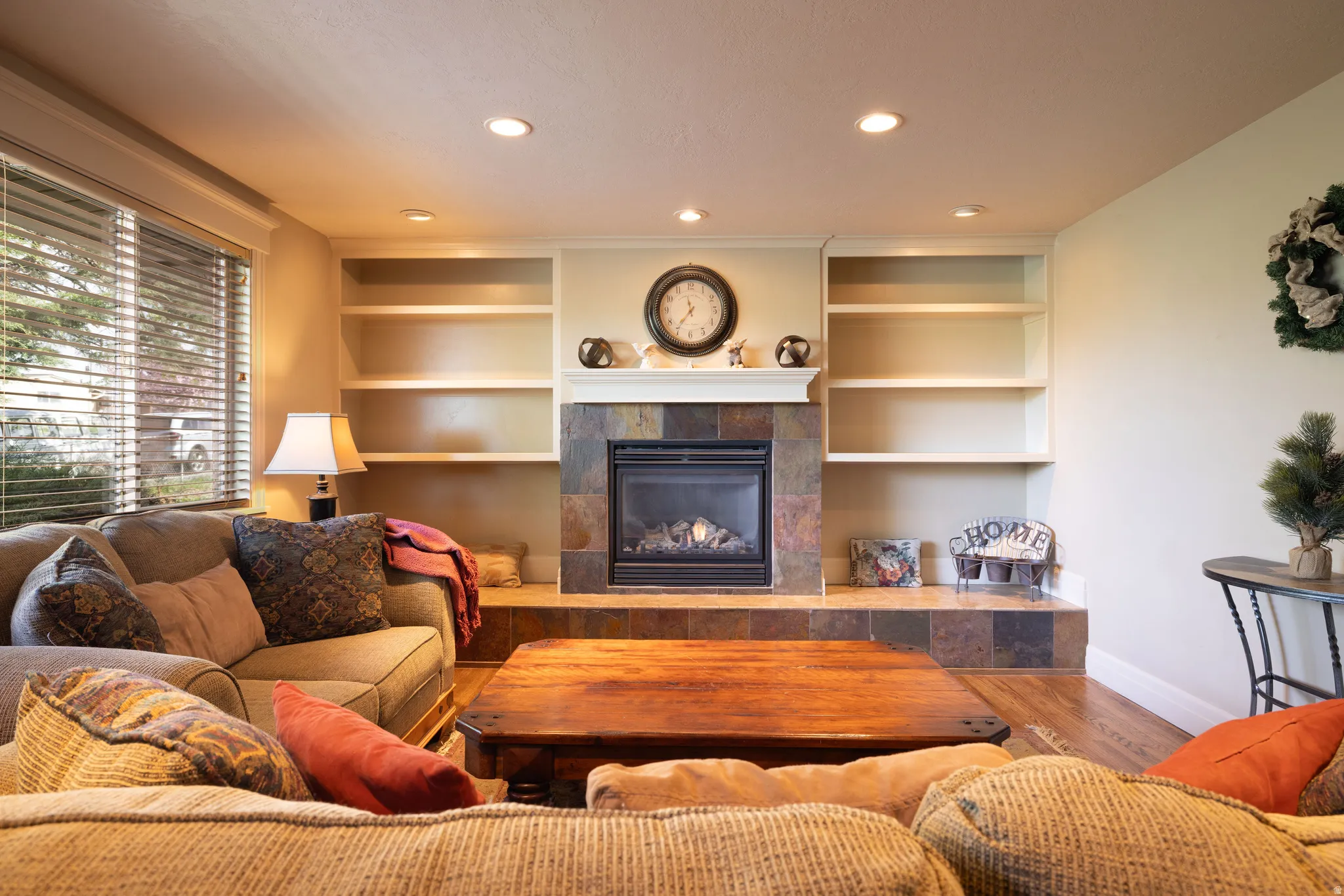 Living room with hardwood floors, a tile fireplace, recessed lighting, and built in shelves