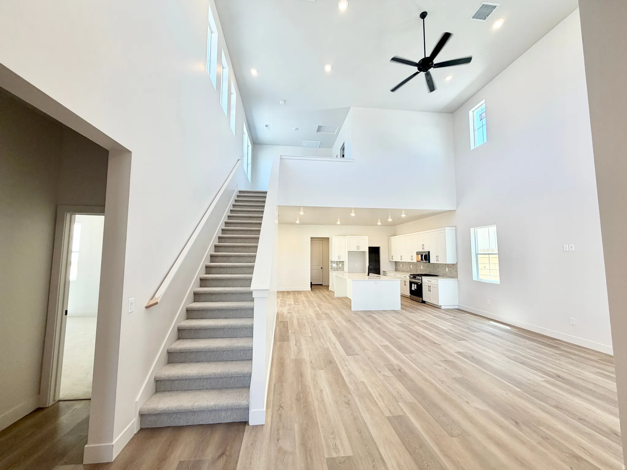 Open-concept living area featuring high ceilings, wood-finish flooring, and a contemporary kitchen with white cabinetry and an island