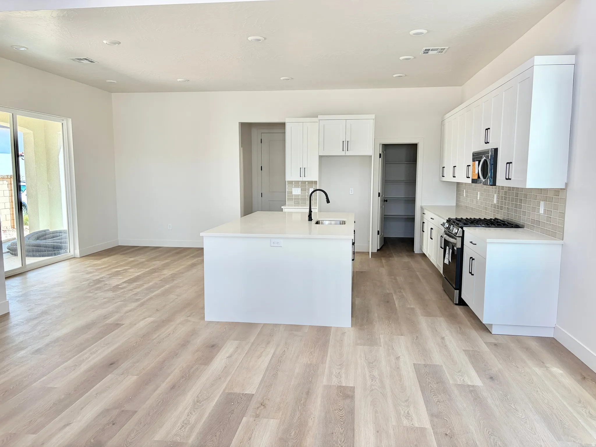 Open-concept kitchen and living area featuring wood-finish flooring, white cabinetry, a kitchen island with sink, a tile backsplash, and sliding glass doors