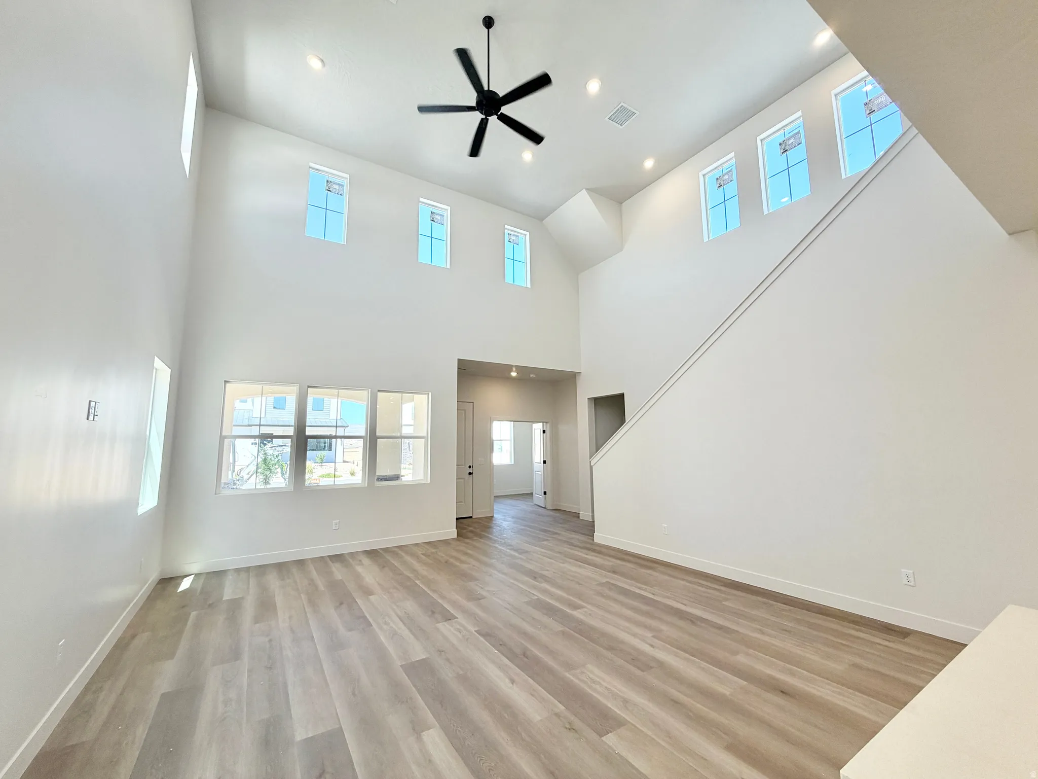 Spacious room featuring vaulted ceilings, wood-finish flooring, a contemporary ceiling fan, recessed lighting, and numerous windows