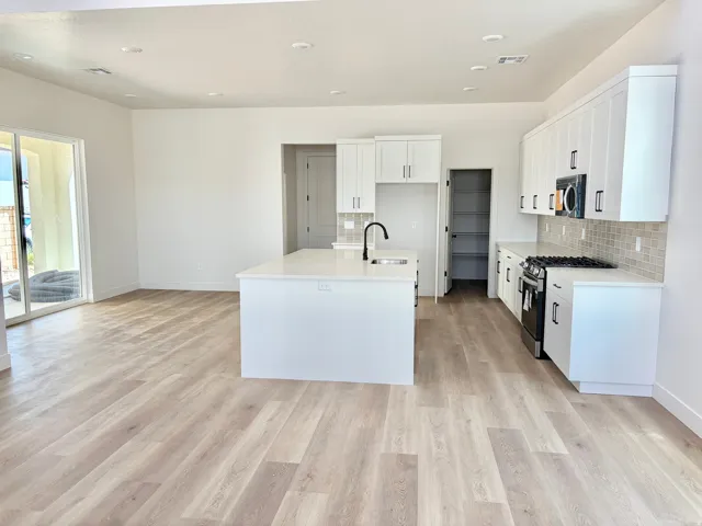 Open-concept kitchen and living area featuring wood-finish flooring, white cabinetry, a kitchen island with sink, a tile backsplash, and sliding glass doors