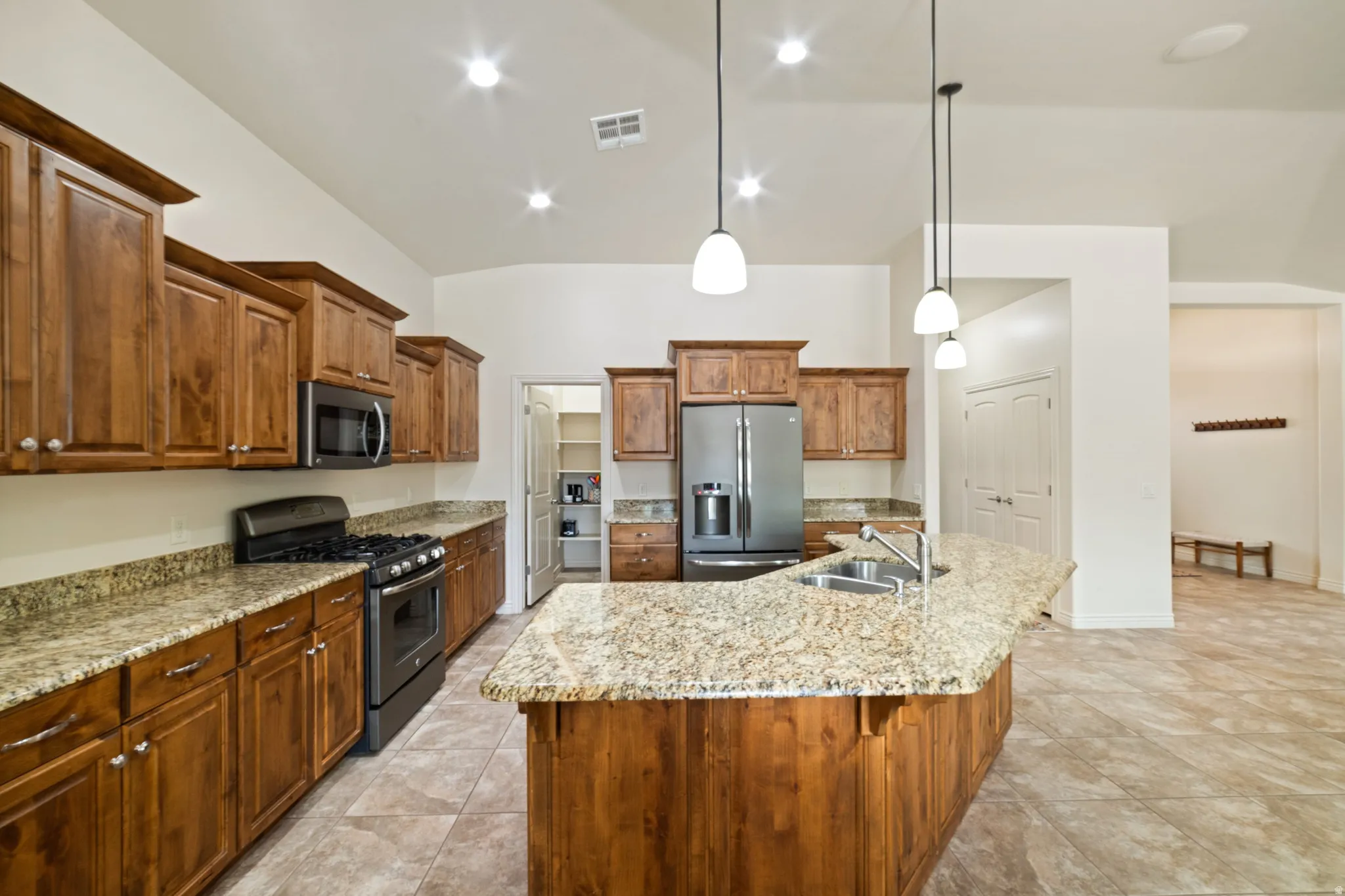 Kitchen featuring stainless steel appliances, light stone countertops, wood finish cabinetry, and hanging light fixtures