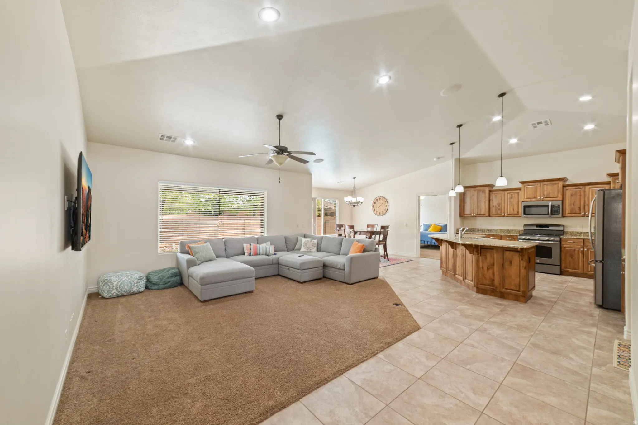 Living room with light colored carpet, lofted ceiling, ceiling fan, light tile patterned floors, and hanging lights