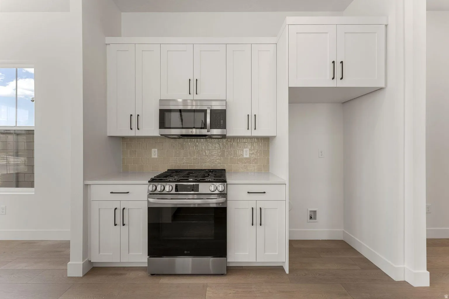 Kitchen with stainless steel appliances, white cabinetry, light wood-style flooring, decorative backsplash, and light stone counters