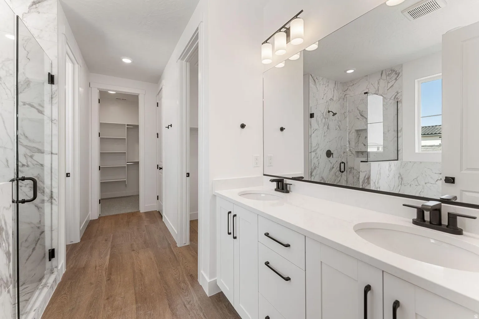 Full bathroom with a marble finish shower, double vanity, a walk in closet, and light wood-style floors