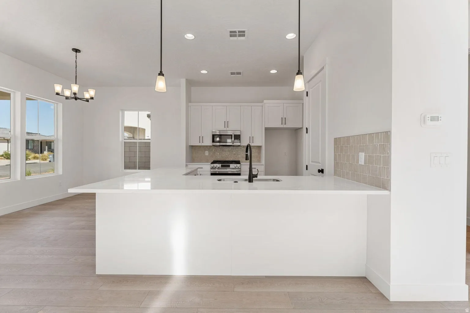 Kitchen featuring white cabinets, decorative backsplash, light stone counters, a peninsula, and stainless steel appliances