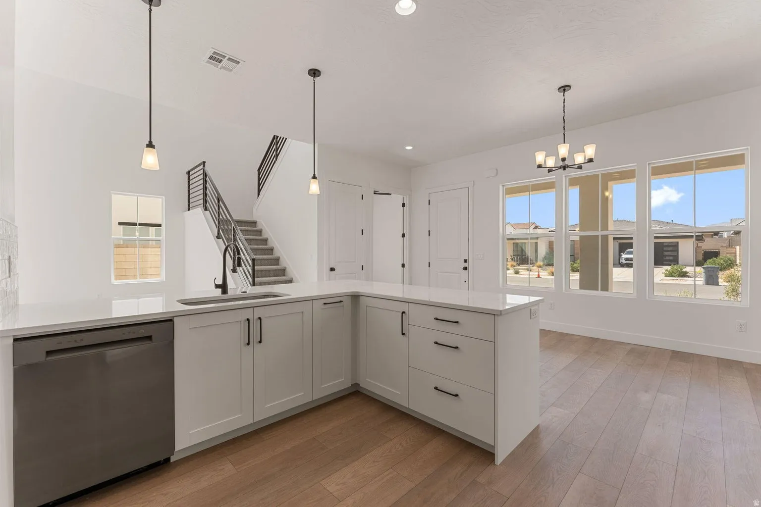 Kitchen with stainless steel dishwasher, light wood finished floors, suspended lighting, light stone counters, and white cabinetry
