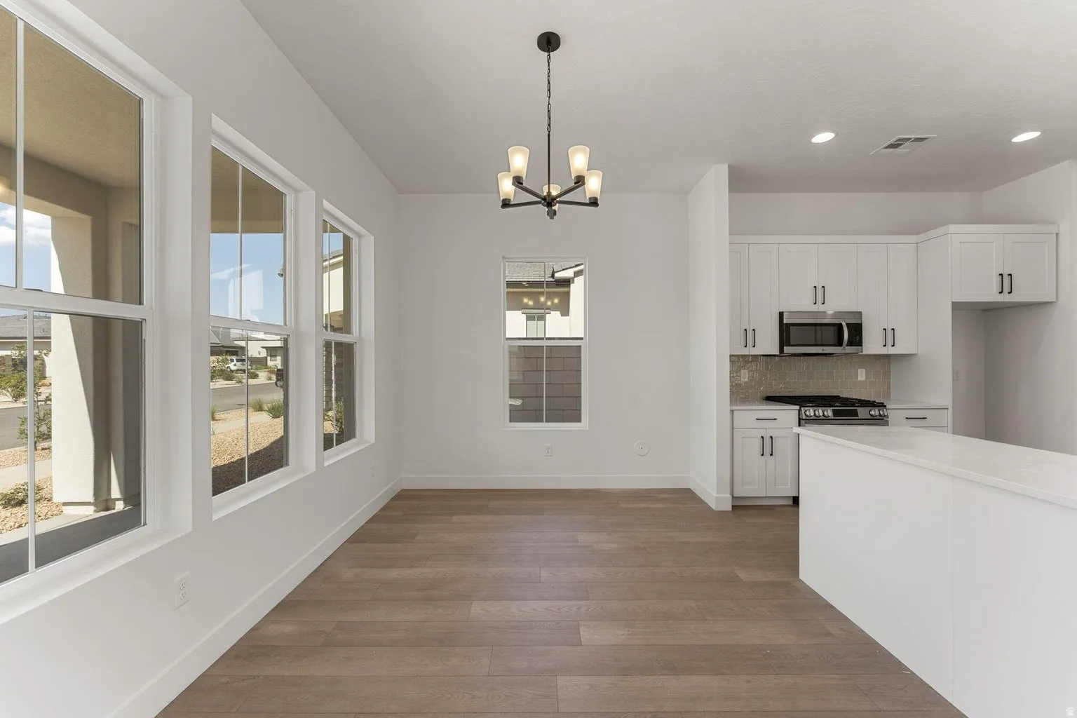 Kitchen with dark wood-style floors, suspended lighting, white cabinets, stainless steel appliances, and backsplash