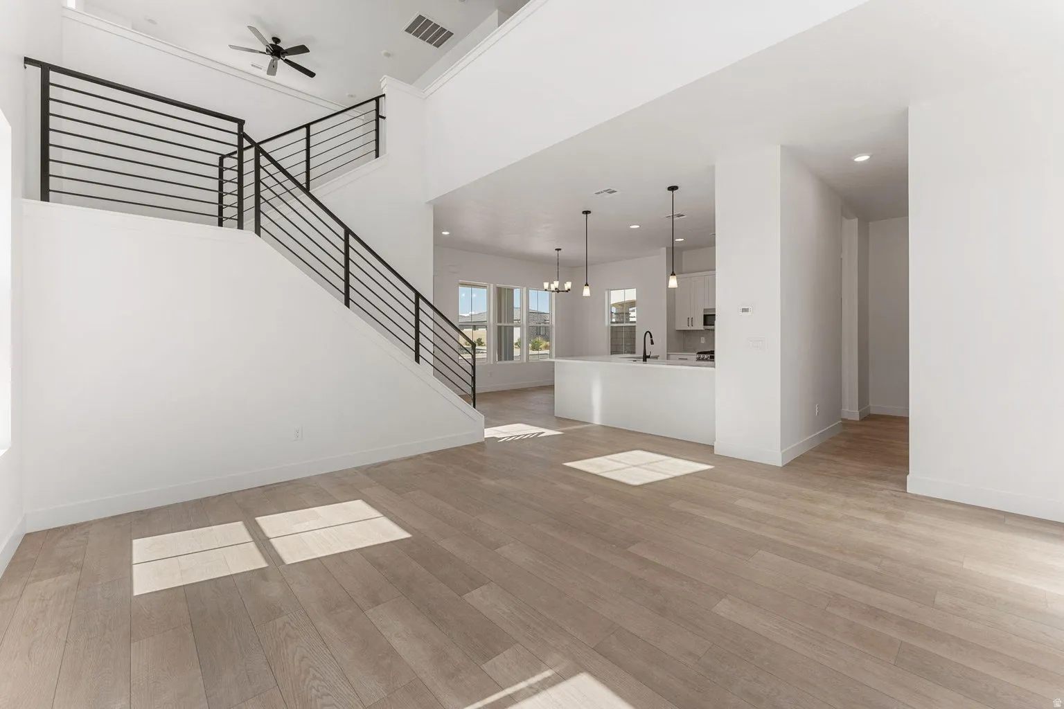 Unfurnished living room with light wood finished floors, a ceiling fan, suspended lighting, and a high ceiling